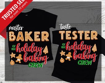 May include: Two black t-shirts with holiday baking designs. One says "Master Baker" and the other says "Taste Tester" in gingerbread-style lettering. The shirts also feature the text "of the holiday baking crew" with gingerbread man and tree graphics.