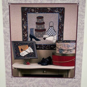 May include: A quilt pattern titled "Crimson & Old Lace" by The Picket Fence, designed by Elle Colquitt. The pattern features a vintage-inspired design with a red and white color scheme. The quilt pattern includes a variety of elements, such as a pair of shoes, a hatbox, and a vintage-style apron.