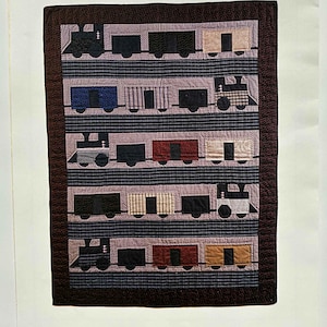 May include: A quilted wall hanging featuring a train design. The quilt showcases various train cars in shades of black, blue, red, and tan, set against a striped background. The word "TRAINS" is at the top.