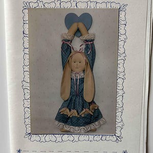 May include: A fabric door knob or peg hanger in the shape of a bunny, wearing a blue polka dot dress with lace trim. The text "Sew Special" and "Upsy Daisy" are visible.