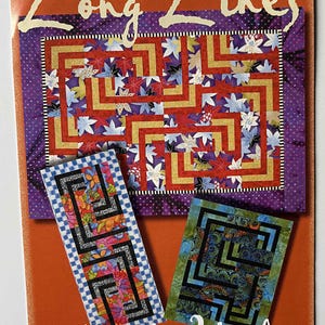 May include: A quilt pattern booklet titled Long Lines by Maple Island Quilts. The cover features a large rectangular quilt with a red and gold maze design over a purple floral background, alongside two smaller rectangular quilt variations.
