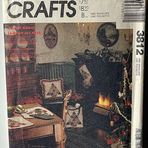 May include: A vintage McCall's Crafts pattern envelope featuring a cozy Christmas scene. The cover displays the text "CRAFTS" and "HOLIDAY MAGIC" with a room decorated for the holidays, including a Christmas tree and fireplace.
