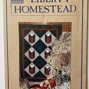 May include: A quilt pattern featuring a quilt block design with a central star and eight surrounding blocks with a stylized angel figure. The quilt is made with red, white, blue, and black fabrics. The pattern is titled "Liberty Homestead".