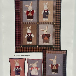 May include: A patchwork quilt and three pillows featuring appliqued rabbits in various outfits. The quilt has a checkered pattern with four rabbit squares. The pillows have rabbit designs with red, blue, and white accents. The text "OLD RABBITS" is at the top.