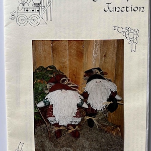 May include: A brochure titled "Ginger Snap Junction" featuring two handmade woodland elves with long white beards, red and black hats, and patterned clothing. The background is a wooden wall.