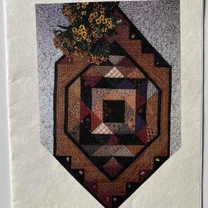 May include: A quilting pattern booklet titled "Table Scraps" with a colorful quilt design on the cover. The quilt is made of various fabrics in shades of brown, red, black, and blue. The booklet is by Tea for Two and has the product code TFT11007.