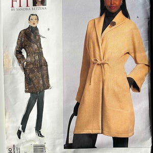 May include: A sewing pattern for a coat, featuring illustrations and a photograph of a woman wearing a tan coat with a tie waist. The pattern includes the text "TODAY'S FIT BY SANDRA BETZINA" and "VOGUE PATTERNS".