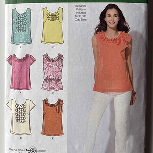 May include: Simplicity sewing pattern 2599, size D5 4, 6, 8, 10, 12. The envelope displays illustrations of six sleeveless and short-sleeve tops with various ruffle and bow details, alongside a photograph of a model wearing an orange sleeveless top.