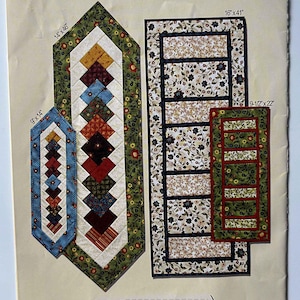 May include: A pattern for "Double Duty Runners" in two sizes. The image shows three quilted table runners with floral and geometric designs. The largest runner is 16" x 41", the medium is 14" x 46", and the smallest is 9-1/2" x 22".