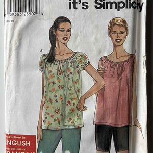 May include: A Simplicity sewing pattern envelope, number 9178, featuring illustrations of two tops with gathered necklines and tie closures. One top has short puff sleeves and a floral print, while the other is sleeveless and solid pink. Includes size A 6-16.