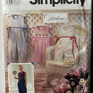 May include: Simplicity sewing pattern featuring children's clothing designs. The pattern includes overalls and a romper, with various fabric options. The image shows the pattern cover with a child's photo and a wicker chair.