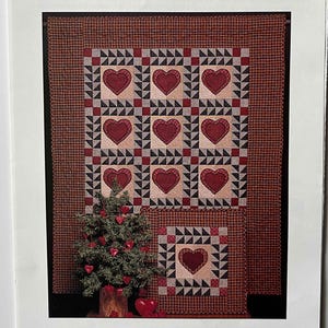 May include: A pattern for a quilt titled "Cinnamon Hearts" featuring a patchwork design with red heart shapes. The design includes a small Christmas tree with heart ornaments. The text "thimbleberries, inc." is also visible.