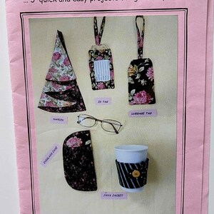 May include: A pink instructional pamphlet titled QUICK GIFTS SWD 243 featuring five fabric projects: a floral napkin, an ID tag, a luggage tag, an eyeglass case, and a striped java jacket with a button, plus a pair of eyeglasses in the center.
