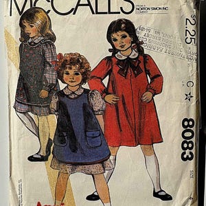 May include: Vintage McCall's sewing pattern featuring illustrations of three young girls in dresses. The pattern, titled "Annie," includes a price of $2.25 and the number 8083. The cover is aged with wear and tear.