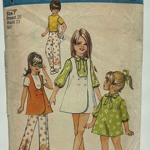 May include: Vintage Simplicity sewing pattern for girls' clothing, featuring illustrations of various outfits. The pattern cover shows a size 7, breast 26 inches, and waist 23 inches. The design includes dresses and pants.