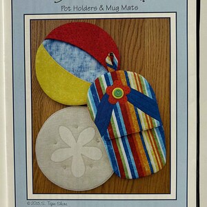 May include: A framed image featuring three fabric pot holders and mug mats. The designs include a beach ball, a flip-flop, and a sand dollar. The text "Seashore Fun!" and "Pot Holders & Mug Mats" are visible.