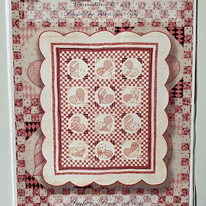 May include: Pink-i-Li-Cious quilt pattern featuring a patchwork design of hearts in shades of pink and red. The pattern is designed by Johná Lee Burk and is finished at 58 inches by 69 inches. The pattern is available from Amber Rose Press, 190 North Main St., Panguitch, UT 84759, (435) 676-8655.