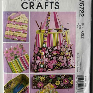 May include: A McCall's Crafts sewing pattern, M5722, featuring a tote bag and accessories. The main bag has a floral and striped design with pink, green, and black colors. Additional accessories include a needle case and a small pouch. The pattern includes the size OSZ.
