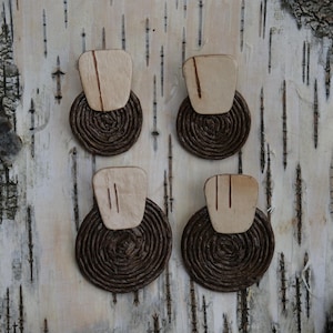 May include: Four pairs of handmade earrings. Each earring features a light-colored, rectangular top with a dark brown, circular base. The earrings are displayed on a textured, light-colored wooden surface.
