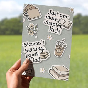 May include: A light gray card with a variety of stickers on it. The stickers feature illustrations of books, flowers, a cup of iced coffee, and text that reads "Mommy's reading, go ask Dad" and "Just one more chapter, kids".