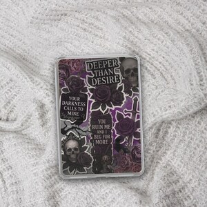 May include: A clear phone case featuring a collage of gothic imagery. The design includes skulls, roses, and text that reads "Deeper Than Desire," "Your Darkness Calls to Mine," and "You Ruin Me and I Beg for More." The color palette is primarily black, purple, and gray.