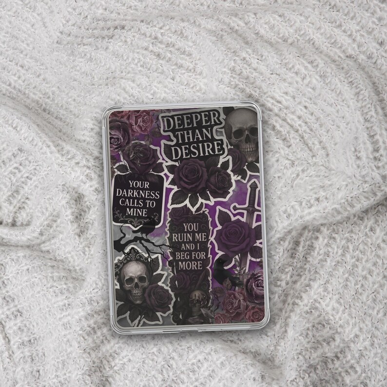 May include: A clear phone case featuring a collage of gothic imagery. The design includes skulls, roses, and text that reads "Deeper Than Desire," "Your Darkness Calls to Mine," and "You Ruin Me and I Beg for More." The color palette is primarily black, purple, and gray.