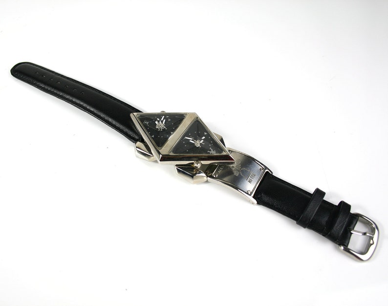 Pu&ograve; includere: Un orologio da polso in pelle nera con un quadrante a forma di diamante a doppia faccia argentato. L'orologio ha un cinturino in pelle nera con una fibbia argentata.