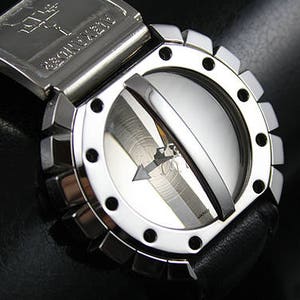Puede incluir: Primer plano de un reloj de pulsera plateado con un diseño único. El reloj presenta una esfera circular con un diseño de flecha central y una cubierta giratoria. La correa es de cuero negro. La palabra "ALEXANDER" es visible en el cierre.