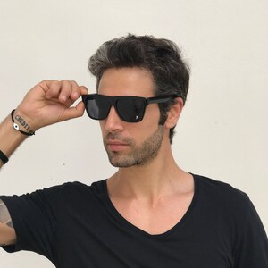 May include: A man wearing black sunglasses with a black t-shirt.