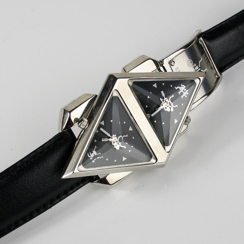 Pu&ograve; includere: Un orologio da polso triangolare argentato con due quadranti neri e un cinturino in pelle nera.