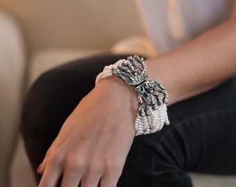 May include: A silver butterfly-shaped clasp with a pearl bracelet. The bracelet is made of multiple strands of small white pearls.