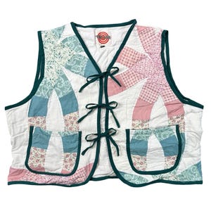 May include: A sleeveless quilted vest featuring a patchwork design of white, teal, and pink floral and checkered fabric patterns. The vest has a dark green trim, three front tie closures, and two front pockets with a label reading Target.