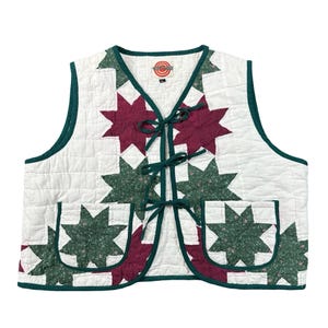 May include: A quilted vest featuring a white background with a repeating star pattern in dark red and floral green. The vest has a dark green trim, three front tie closures, and two square patch pockets. A label with a target logo reads XL.
