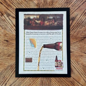 May include: A framed vintage Tecate beer advertisement featuring a bar scene, a map of Mexico, and a bottle pouring beer. The text reads: Men have been known to ride a long way for a beautiful woman or an ice cold Tecate. Or both. The print is in a black frame.