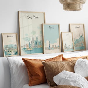 May include: A collection of framed art prints featuring cityscapes. The prints include the names of cities such as New York, Paris, London, Istanbul, and Barcelona. Each print has a light-colored wooden frame and a watercolor-style illustration.