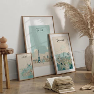 May include: Three framed art prints featuring watercolor illustrations of cityscapes. The prints showcase the skylines of Istanbul, Paris, and Barcelona, each labeled with its respective city name. The frames have a natural wood finish, and the artwork has a soft, muted color palette.
