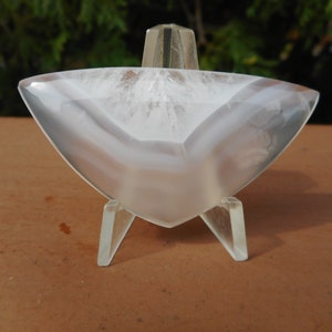 May include: A white agate slice with a translucent, cloudy appearance. The slice is displayed on a clear plastic stand.