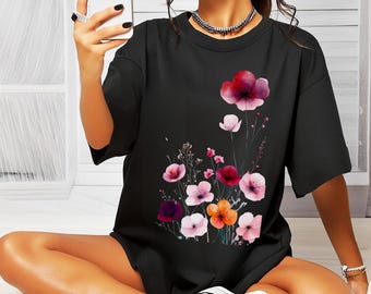 May include: Black short-sleeved t-shirt featuring a floral design with pink, red, and orange flowers. The flowers are clustered on the front of the shirt. The shirt is worn by a person.