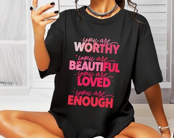 May include: Black t-shirt with the words "You are Worthy, Beautiful, Loved, Enough" in pink and white lettering. The shirt has a crew neck and short sleeves.