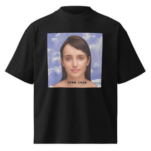 May include: A black short-sleeve t-shirt featuring a square graphic print on the chest. The print displays a portrait of a person with brown hair against a blue sky with white clouds. The text "free base" is printed in black letters on the neck.