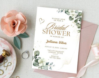 May include: A bridal shower invitation with floral and eucalyptus details. The invitation includes the text "Bridal Shower" and details for Juliana Silva's shower. A paper flower, ring, and stationery are arranged on a light surface.