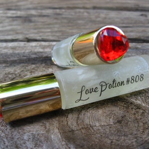 May include: Two clear glass bottles with gold caps and red gemstone tops. The bottles are labeled "Love Potion #808".