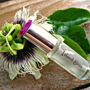 May include: A clear glass roller bottle with a silver cap and the text "Island Bliss" on the label. The bottle is resting on a white flower with green leaves.