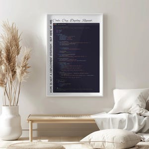 May include: A framed print with the text "Code. Cry. Deploy. Repeat." and "HOPE IS NOT A DEPLOYMENT STRATEGY... BUT HERE WE ARE." The print features computer code on a dark background. The frame is white, and the print is displayed on a wall.
