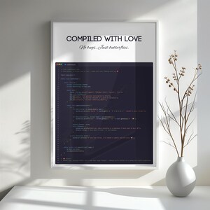 Pode incluir: Uma impress&atilde;o emoldurada com o texto "COMPILED WITH LOVE" e "No bugs. Just butterflies." A impress&atilde;o apresenta um fundo escuro com linhas de c&oacute;digo. Um vaso branco com galhos est&aacute; &agrave; direita.