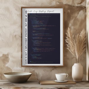 May include: A framed print featuring the text "Code. Cry. Deploy. Repeat." and "HOPE IS NOT A DEPLOYMENT STRATEGY... BUT HERE WE ARE." The print shows lines of code on a dark background. The frame is brown, and the print is displayed on a neutral-toned wall.