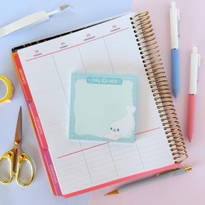 May include: A planner with a gold spiral binding, open to a weekly spread. A light blue sticky note with the text "Seally little notes" and a seal illustration is on the page. Pens, scissors, and tape are also visible.
