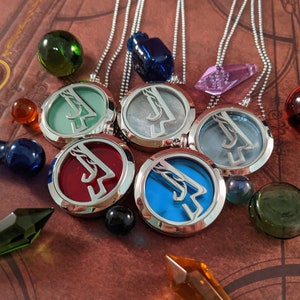 May include: A collection of silver-toned pendant necklaces with colorful, circular inserts. The pendants are arranged with various glass beads and crystal shapes on a brown, patterned surface. The pendants have red, blue, green, and gray inserts.