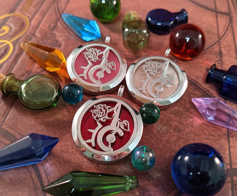 May include: An assortment of decorative items including three silver-rimmed pendants with a rose and script design, glass bottles, and colorful crystal-shaped and spherical objects. The pendants have red and light-colored backgrounds. The objects are arranged on a brown surface.