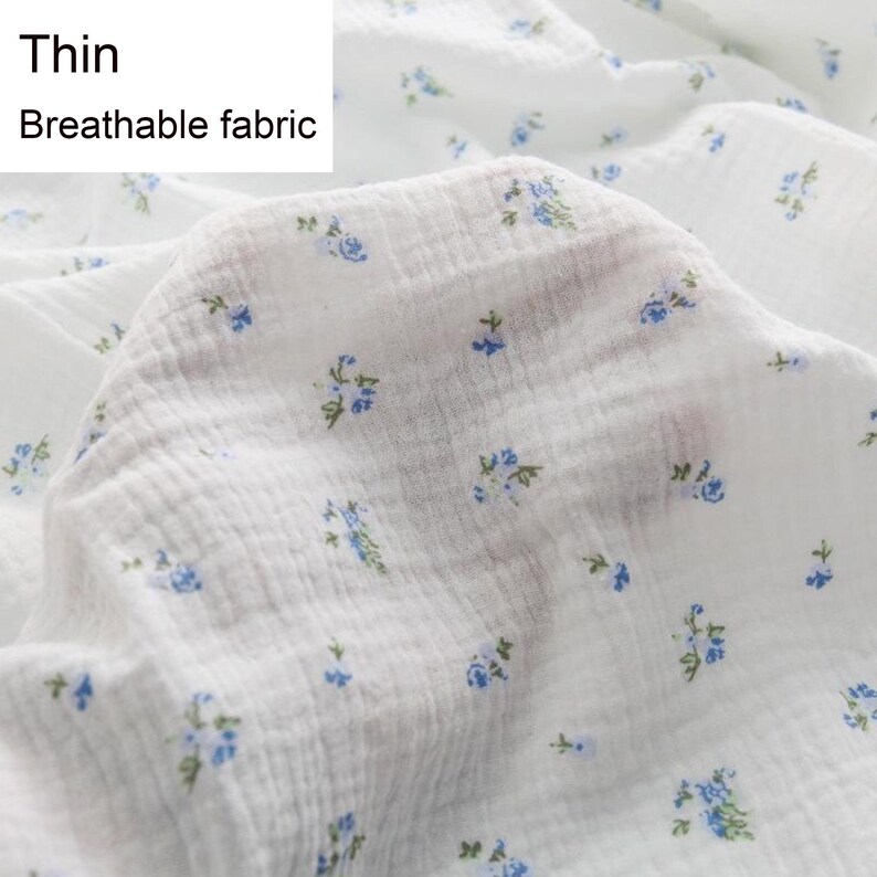 Op de afbeelding: Witte katoenen stof met een klein blauw bloemenpatroon. De stof is dun en ademend. De tekst "Thin Breathable fabric" is zichtbaar in de linkerbovenhoek van de afbeelding.